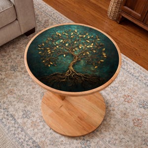 May include: A round wooden side table with a teal and gold tree of life design on the tabletop. The tree features gold leaves and roots against a teal background. The table has a light wood base and a round pedestal.