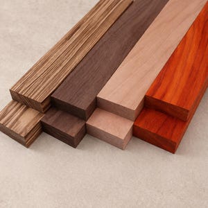 May include: An assortment of wooden planks in various colors and grain patterns. The planks range from light tan to dark brown and reddish-orange, showcasing the natural beauty of the wood. The planks are stacked at different levels.