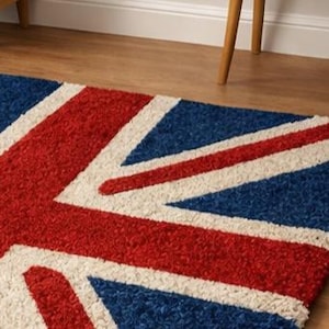 Puede incluir: Una alfombra rectangular con la bandera del Reino Unido, la Union Jack. El dise&ntilde;o incluye colores rojo, blanco y azul. La alfombra est&aacute; colocada sobre un suelo de madera, con patas de muebles visibles en el fondo.