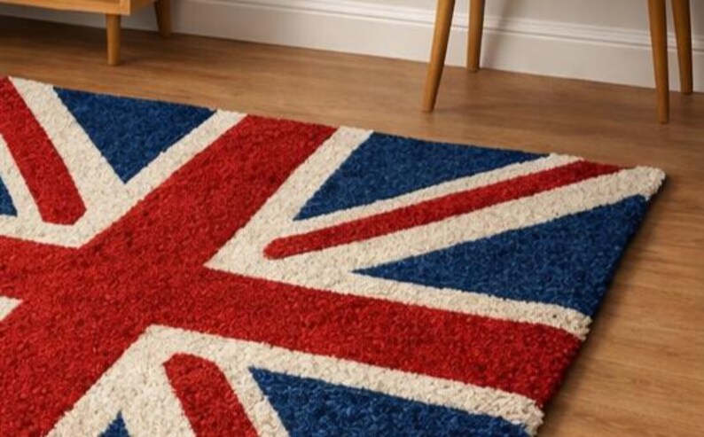 Puede incluir: Una alfombra rectangular con la bandera del Reino Unido, la Union Jack. El dise&ntilde;o incluye colores rojo, blanco y azul. La alfombra est&aacute; colocada sobre un suelo de madera, con patas de muebles visibles en el fondo.