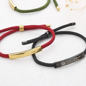May include: Close-up of several bracelets with rope-like bands in red, black, and green. Each bracelet has a gold-coloured metal bar or accents. One black bracelet has a medical ID tag that reads "Type 1 Diabetic Insulin Pump."