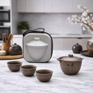Puede incluir: Un juego de té marrón con tres tazas pequeñas, una tetera y un estuche de transporte. La tetera tiene tapa y boquilla, con caracteres asiáticos. Las tazas y la tetera son de color a juego.