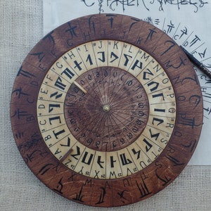 May include: A wooden circular alphabet wheel with a rotating dial and a black pencil. The wheel has a brown outer ring with black letters and a lighter wood inner ring with black numbers.