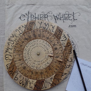 Może przedstawiać: Drewniana szyfrówka z okrągłym wzorem i obracającym się tarczą. Szyfrówka wykonana jest z dwóch różnych rodzajów drewna, a tarcza jest oznaczona literami i symbolami. Szyfrówka służy do kodowania i dekodowania wiadomości.