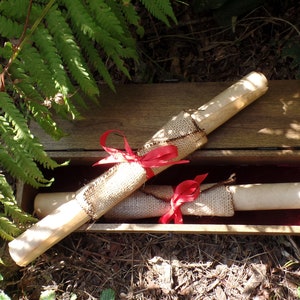 May include: Two rolled up scrolls tied with red ribbon and burlap, inside a wooden box with a red velvet lining.