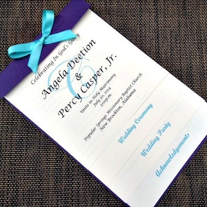 May include: A wedding program with a purple border and a teal ribbon. The program features the names Angela Deetion and Percy Casper, Jr., along with the wedding date and location. The text "Celebrating In God's Glory" is also visible.