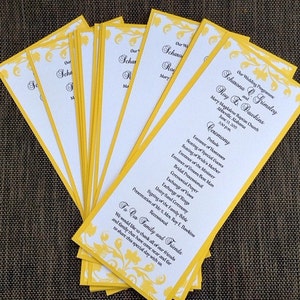 May include: A stack of yellow and white wedding programs with a floral design. The program lists the wedding ceremony for Scharona Q. Grimsley and Roy F. Dawkins, taking place on June 13, 2015 at 3:30 PM at Mary Magdalene Baptist Church in Abbeville, Massachusetts.