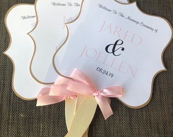 May include: Three white wedding fans with gold trim and pink ribbon. The top fan says "Welcome to the Marriage Ceremony of Jared & Joellen 08.24.19".