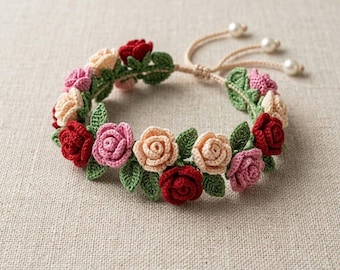 Puede incluir: Una pulsera de ganchillo con diseño floral. Presenta rosas rojas, rosas y melocotón, complementadas con hojas verdes. El cierre ajustable es de hilo beige y tiene tres perlas. Un accesorio encantador.