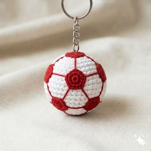 Puede incluir: Un llavero de fútbol hecho a mano con ganchillo. La pelota presenta un diseño clásico con paneles blancos y rojos, unido a una cadena y un llavero de color plateado. Un accesorio encantador para los aficionados al deporte.