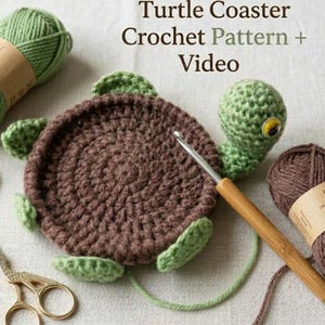 May include: A crocheted turtle coaster with green flippers and head, and a brown shell. The image includes a crochet hook, scissors, and yarn. Text reads "Turtle Coaster Crochet Pattern + Video."
