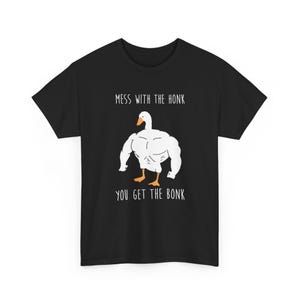 May include: A black short-sleeve t-shirt featuring a graphic of a muscular white goose with an orange beak and feet. The text above the goose reads "MESS WITH THE HONK" and the text below the goose reads "YOU GET THE BONK" in white lettering.