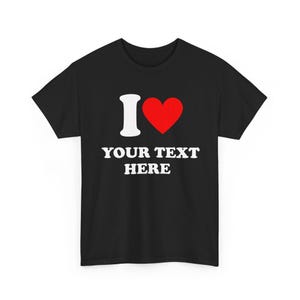 Op de afbeelding: Zwart T-shirt met een witte "I" gevolgd door een rood hartsymbool en de tekst "YOUR TEXT HERE" in het wit. Het shirt heeft een ronde hals.