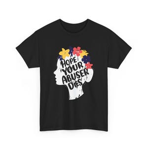 May include: A black short-sleeved t-shirt featuring a white silhouette of a human head in profile. The head is adorned with a crown of colorful flowers in yellow, blue, and red. The text HOPE YOUR ABUSER DIES is printed in black across the silhouette.