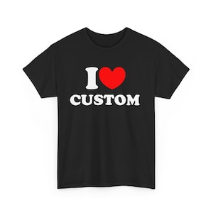 Può includere: T-shirt nera con la scritta "I ♥ CUSTOM". La "I" è bianca, il cuore è rosso e la parola "CUSTOM" è bianca. Il design è stampato su una t-shirt girocollo, un capo casual popolare.