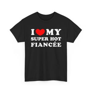 Puede incluir: Camiseta negra con el texto blanco "I ❤️ MY SUPER HOT FIANCÉE", con un corazón rojo en lugar de la palabra "love". Una camiseta informal para un prometido/a.