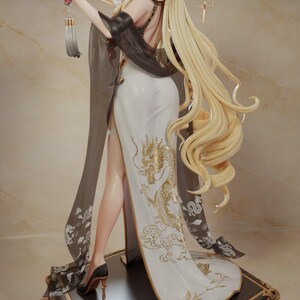 以下が含まれることがあります： 白いドレスに金色のドラゴンのデザインが施された女性の精巧なフィギュア。扇子を持ち、長い金髪です。ベースは黒と金のアクセント。フィギュアの高さは約30cmです。