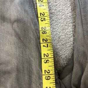 May include: Close-up of gray denim jeans with a yellow measuring tape showing a length of 23 to 30 inches. The jeans are a solid gray color and appear to be new or gently used.