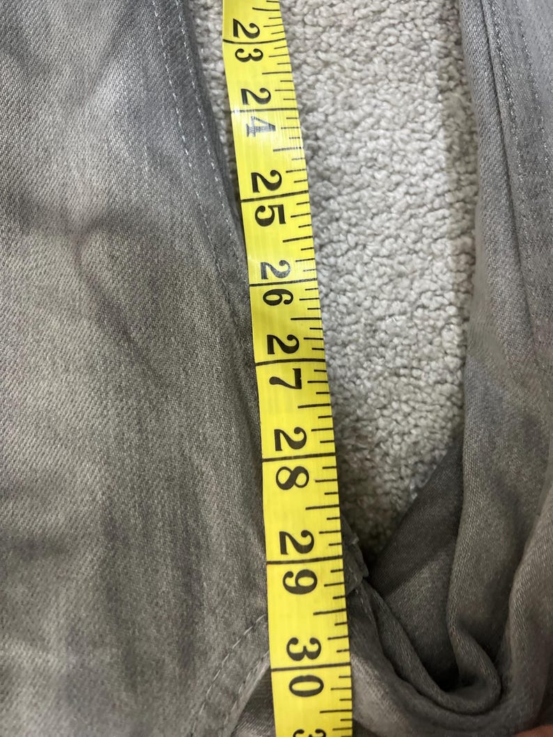 May include: Close-up of gray denim jeans with a yellow measuring tape showing a length of 23 to 30 inches. The jeans are a solid gray color and appear to be new or gently used.