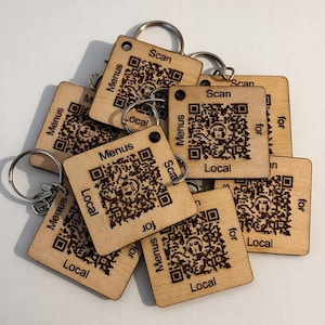Puede incluir: Un conjunto de llaveros de madera cuadrados con códigos QR y las palabras "Menus", "Local" y "Scan for". Cada llavero tiene un anillo metálico. La madera es de color claro.