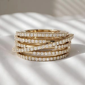 May include: A gold ring featuring a multi-layered, wrap-around design. The band consists of several interconnected loops, each encrusted with a continuous row of small, clear, round-cut stones that create a sparkling, textured appearance.