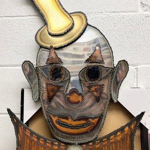 May include: A metal clown face wall decor with a mirrored surface and a bow tie. The clown has a large, yellow hat and a red nose. The text on the sign reads "el Mirror" is to be standing on the floor to create a dramatic appeal in any room of your home or office.