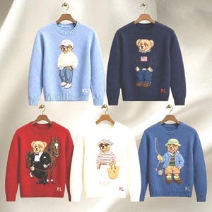 Può includere: Cinque maglioni a maniche lunghe con girocollo in azzurro, blu navy, rosso, bianco e blu medio. Ogni maglione presenta un motivo lavorato a maglia di un orsacchiotto vestito con diversi abiti, con le lettere RL ricamate vicino all'orlo inferiore.
