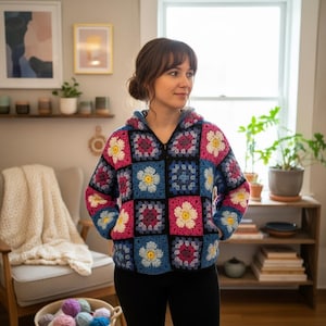 May include: A colorful, crocheted hooded jacket with a floral pattern. The jacket features a patchwork design with squares of blue, pink, and white, creating a vibrant and cozy look. The jacket has a zipper closure and a hood.