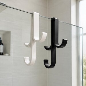 Peut inclure: Deux crochets pour paroi en verre, un blanc et un noir, chacun doté d'un design à double crochet avec un long bras vertical qui s'accroche sur le bord supérieur d'un panneau en verre et deux petits crochets incurvés à différentes hauteurs.