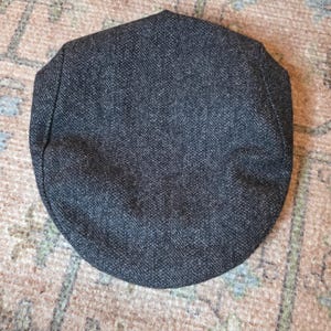 以下が含まれることがあります： ダークグレーのツイードニュースボーイキャップ。丸みを帯びたクラウンと短く硬いブリムが特徴です。生地には微妙なヘリンボーン柄があります。このクラシックスタイルは様々な場面に適しており、ヴィンテージ感を添えます。