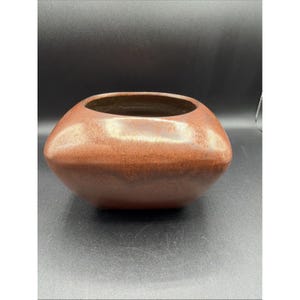 May include: A low, wide ceramic bowl with a rounded square shape and a smooth, matte finish. The exterior features a gradient of warm, earthy brown tones, transitioning from a lighter, speckled reddish-brown at the top to a darker, solid brown base.