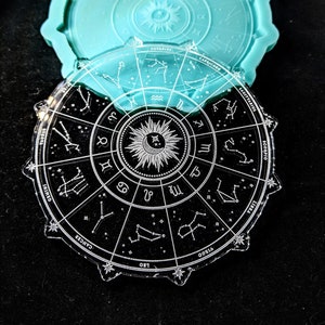 May include: A clear acrylic zodiac wheel with the constellations and names of each sign. The wheel is surrounded by a black background.