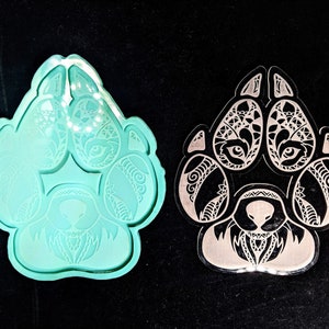 Könnte beinhalten: Eine türkisfarbene Pfotenabdruckform und ein klarer Pfotenabdruck-Ausschnitt mit komplizierten Stammesdesigns. Die Pfotenabdrücke weisen detaillierte Muster und Augenmotive auf, die sich für Bastel- oder Dekorationszwecke eignen.