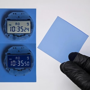 May include: Two digital watches displaying the time, with a blue square held by a gloved hand. The watches show the time as 10:35:24 and 10:35:50. The square is a light blue color.