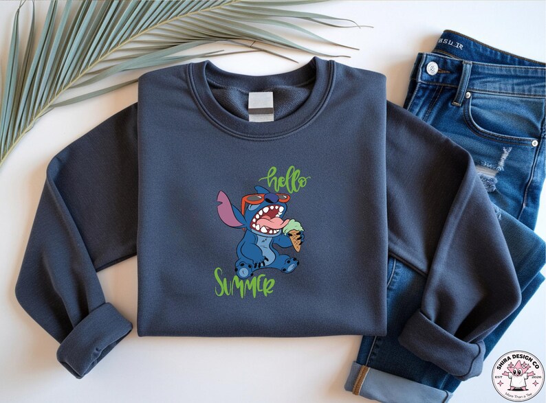 May include: A dark grey sweatshirt with a cartoon character wearing sunglasses and eating ice cream, with the words "hello summer" in green script. The sweatshirt is paired with blue jeans.