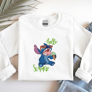 May include: White sweatshirt with a cartoon Stitch design, wearing sunglasses and eating ice cream. Green script reads "hello" and "summer". The sweatshirt is shown with blue denim jeans.
