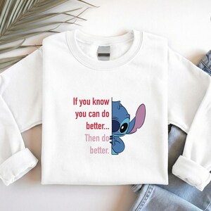 May include: White long-sleeve sweatshirt featuring a blue cartoon character and the text "If you know you can do better... Then do better." The design includes a logo in the upper right corner. The sweatshirt is paired with blue jeans.