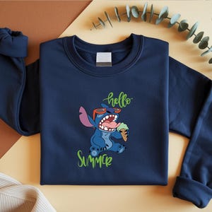 May include: Navy blue sweatshirt with a cartoon Stitch character wearing sunglasses and holding an ice cream cone. The words "hello" and "summer" are written in green script. The sweatshirt has a crew neck and long sleeves.