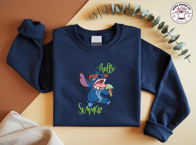 May include: Navy blue sweatshirt with a cartoon Stitch character wearing sunglasses and holding an ice cream cone. The words "hello" and "summer" are written in green script. The sweatshirt has a crew neck and long sleeves.