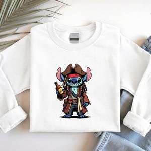 May include: White sweatshirt featuring a cartoon character dressed as a pirate, holding a bottle. The character is blue with brown dreadlocks, wearing a brown pirate hat and coat. The design is centered on the front of the long-sleeved shirt.