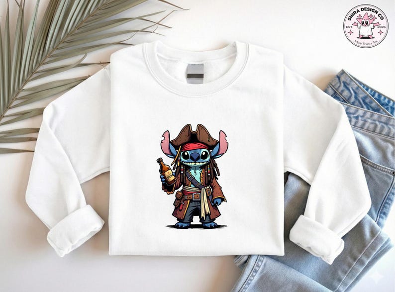 May include: White sweatshirt featuring a cartoon character dressed as a pirate, holding a bottle. The character is blue with brown dreadlocks, wearing a brown pirate hat and coat. The design is centered on the front of the long-sleeved shirt.