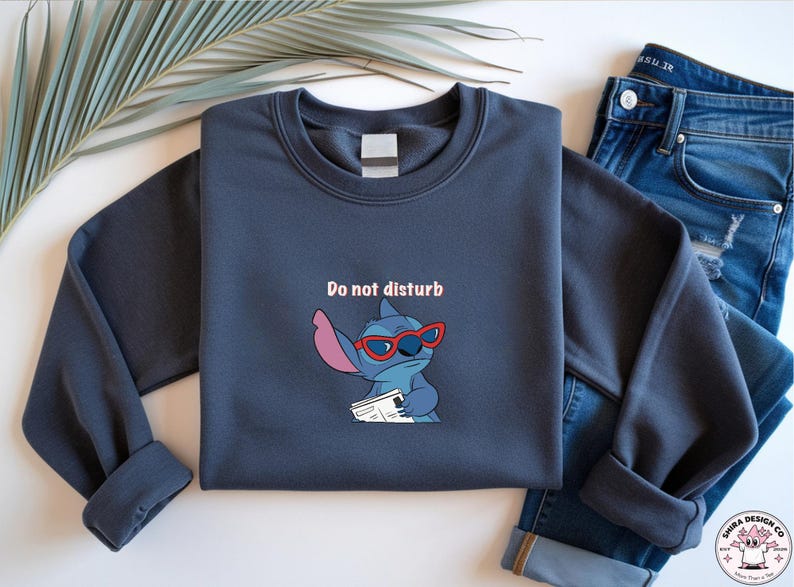 Peut inclure: Un sweat-shirt bleu marine avec un personnage de dessin anim&eacute; Stitch portant des lunettes de soleil rouges et tenant un journal. Le texte "Do not disturb" est au-dessus du personnage. Le sweat-shirt est associ&eacute; &agrave; un jean bleu.