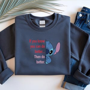 May include: A navy blue sweatshirt featuring a cartoon character and the text "If you know you can do better... Then do better." The sweatshirt is paired with blue jeans. The design is a fun and motivational statement.