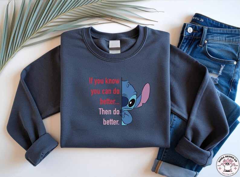May include: A navy blue sweatshirt featuring a cartoon character and the text "If you know you can do better... Then do better." The sweatshirt is paired with blue jeans. The design is a fun and motivational statement.