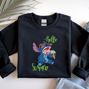 May include: Black crew neck sweatshirt with a cartoon character wearing sunglasses and holding an ice cream cone. The words "hello" and "summer" are written in green script. The sweatshirt is paired with blue jeans.