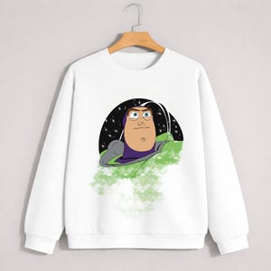 May include: White crew neck sweatshirt featuring a cartoon illustration of Buzz Lightyear from Toy Story. The graphic shows Buzz in his space suit against a starry background. The sweatshirt is a casual, comfortable style.
