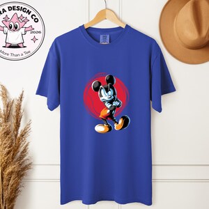 May include: Royal blue t-shirt with a cartoon Mickey Mouse illustration set against a red circle. The shirt is displayed on a wooden hanger. The brand logo is visible on the upper left.