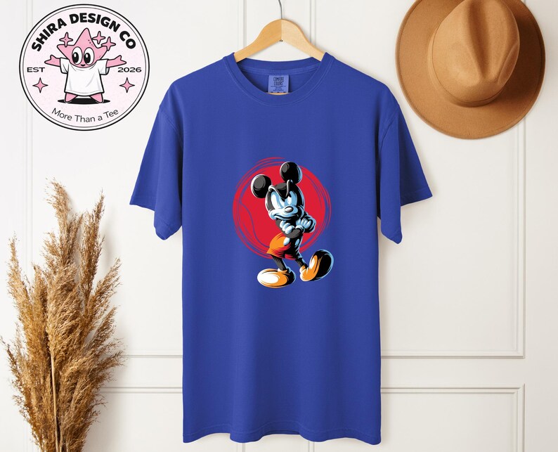 May include: Royal blue t-shirt with a cartoon Mickey Mouse illustration set against a red circle. The shirt is displayed on a wooden hanger. The brand logo is visible on the upper left.