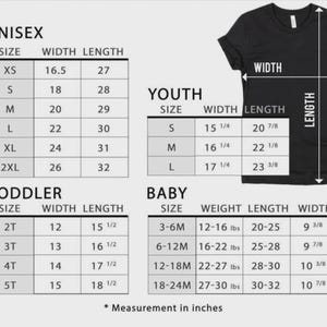 Op de afbeelding: Een zwart t-shirt met een maattabel voor unisex, jeugd, peuter en baby maten. De tabel bevat afmetingen in inches voor breedte en lengte, en gewicht voor babymaten.