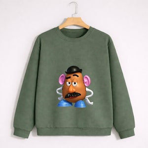 Può includere: Felpa verde con un'immagine a cartoni animati di Mr. Potato Head. Il personaggio ha un viso marrone, baffi neri, cappello nero, orecchie rosa e scarpe blu. La felpa è di colore verde unito.
